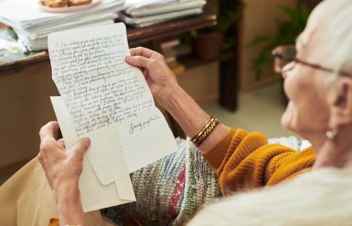 Elderly person reading an intricately handwritten letter, sitting beside a cozy desk filled with stacked papers and plants, expressing emotions of nostalgia and longing while reminiscing